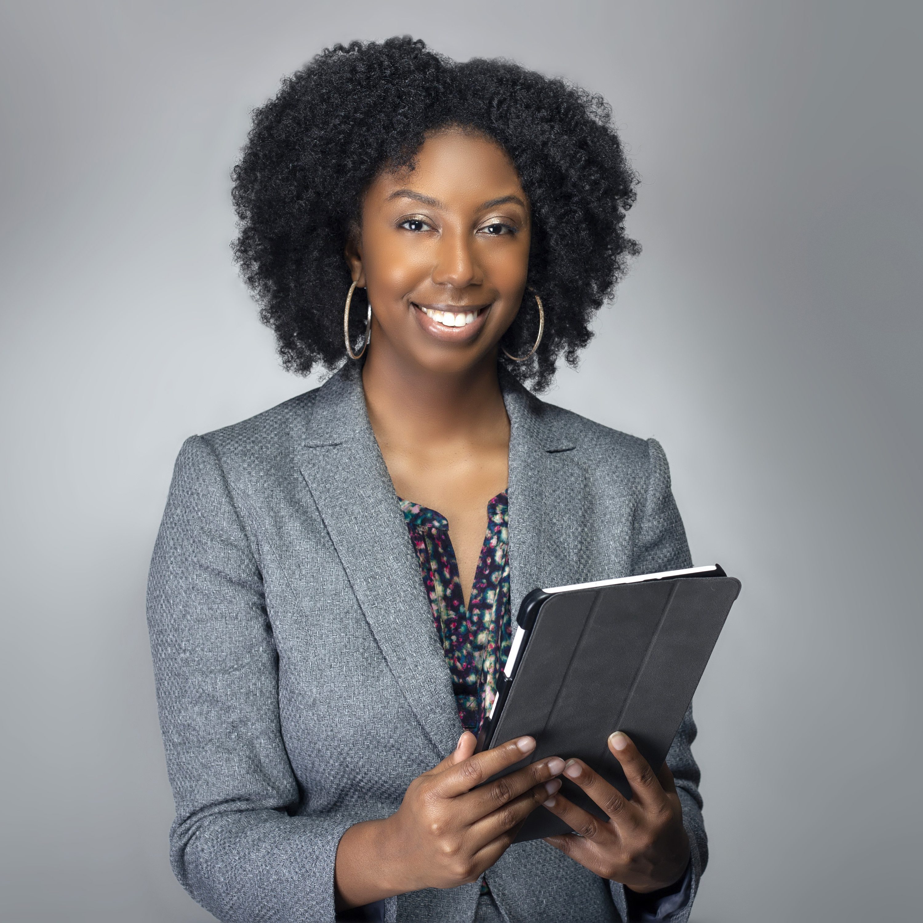 Black African American teacher or businesswoman sitting and holding a tablet computer.  The confident female author or writer looks like she is preparing for a seminar or as a keynote speaker.